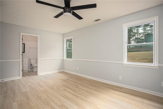 unfurnished room featuring a healthy amount of sunlight, visible vents, a textured ceiling, and light wood finished floors