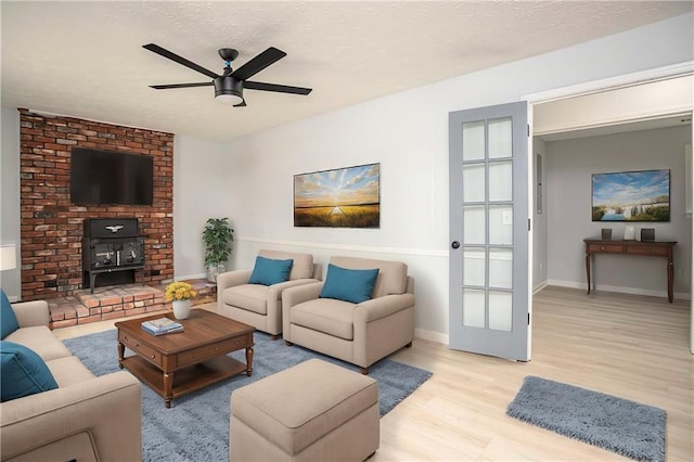 living room featuring a textured ceiling, ceiling fan, a wood stove, and light wood-style floors