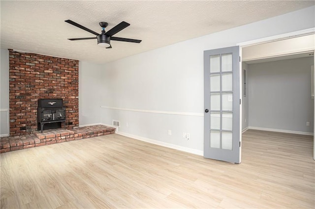 unfurnished living room featuring a wood stove, ceiling fan, a textured ceiling, wood finished floors, and baseboards