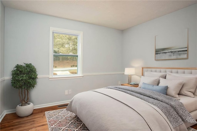 bedroom with baseboards, visible vents, and wood finished floors