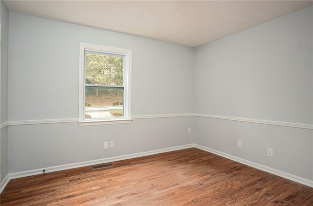 spare room with baseboards, a textured ceiling, visible vents, and wood finished floors