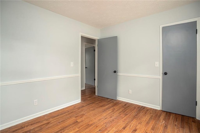 unfurnished bedroom featuring a textured ceiling, wood finished floors, and baseboards