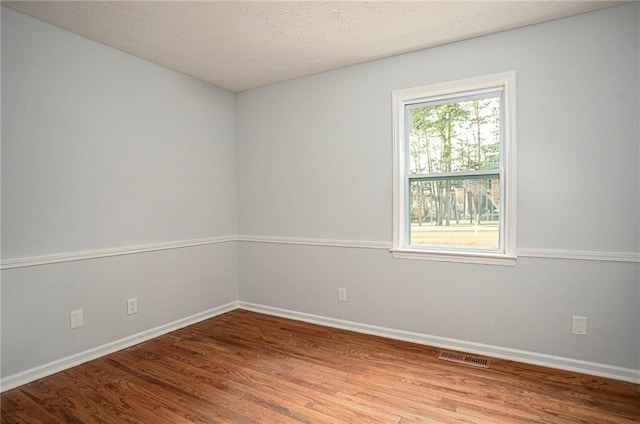 empty room featuring a textured ceiling, wood finished floors, visible vents, and baseboards