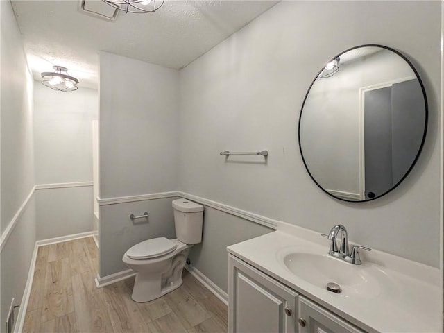 full bath with toilet, a textured ceiling, vanity, wood finished floors, and baseboards