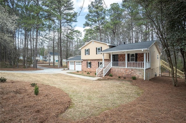 split level home with a garage, driveway, a porch, and brick siding