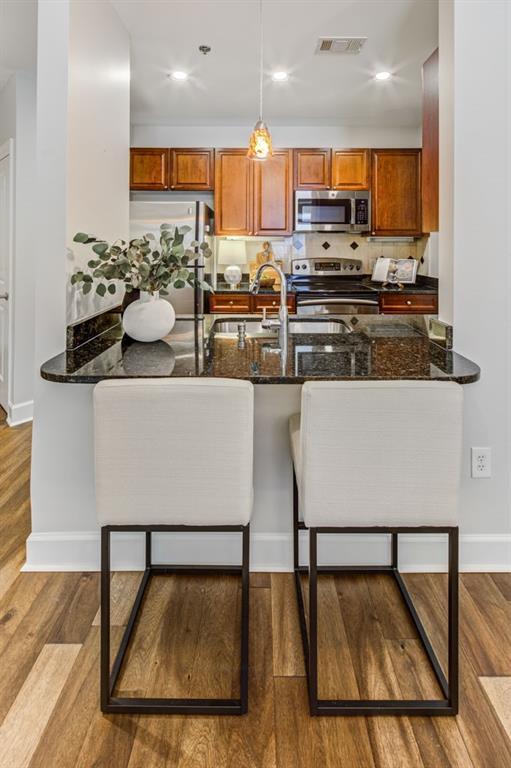 325 E Paces Ferry Rd NE Unit 410, Atlanta, GA 30305 - kitchen with appliances with stainless steel finishes, brown cabinets, baseboards, wood finished floors, and dark stone countertops