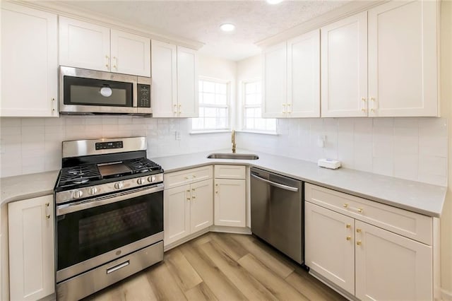 kitchen with a sink, white cabinetry, light wood-style floors, light countertops, and appliances with stainless steel finishes