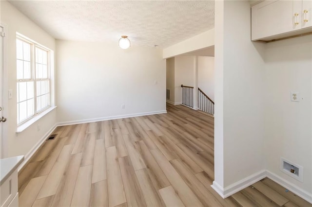 unfurnished room with baseboards, light wood-style flooring, visible vents, and a textured ceiling