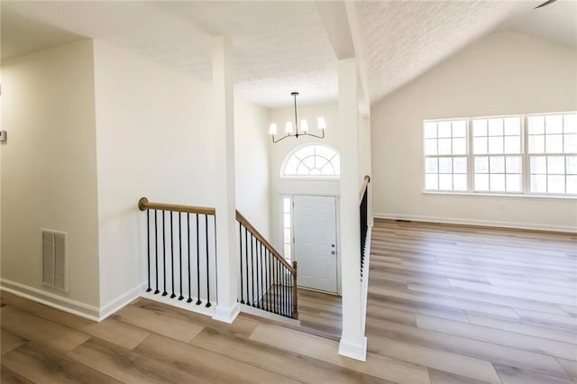 foyer with visible vents, a textured ceiling, wood finished floors, a chandelier, and baseboards