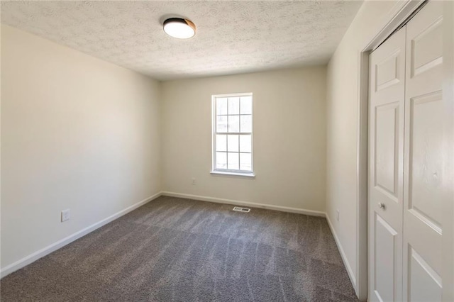 unfurnished bedroom with baseboards, visible vents, dark colored carpet, and a textured ceiling