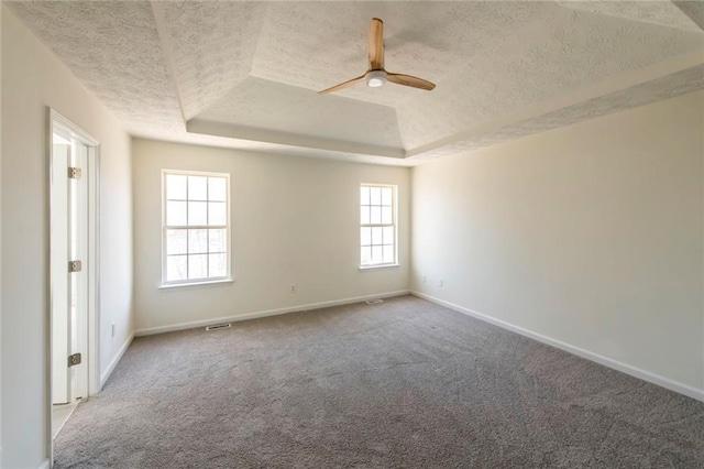 carpeted empty room featuring baseboards, visible vents, ceiling fan, a tray ceiling, and a textured ceiling