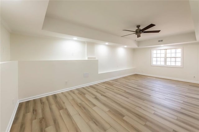 unfurnished room featuring light wood-type flooring, baseboards, visible vents, and a raised ceiling