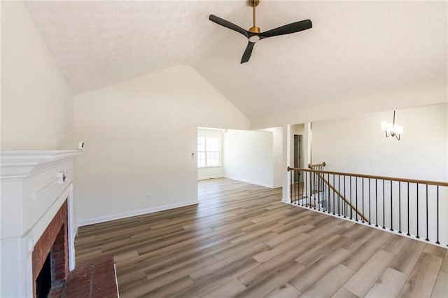 unfurnished living room with lofted ceiling, ceiling fan with notable chandelier, a fireplace, wood finished floors, and baseboards