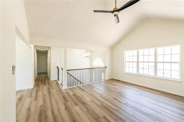 unfurnished room with lofted ceiling, a textured ceiling, ceiling fan with notable chandelier, baseboards, and light wood finished floors