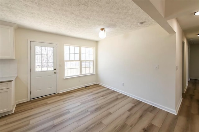 interior space featuring light wood-type flooring, baseboards, and a textured ceiling