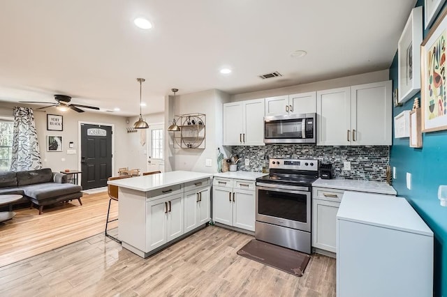 kitchen with kitchen peninsula, stainless steel appliances, white cabinets, hanging light fixtures, and a breakfast bar area