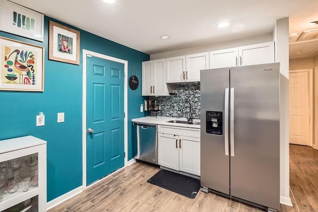 kitchen with appliances with stainless steel finishes, tasteful backsplash, sink, light hardwood / wood-style flooring, and white cabinets