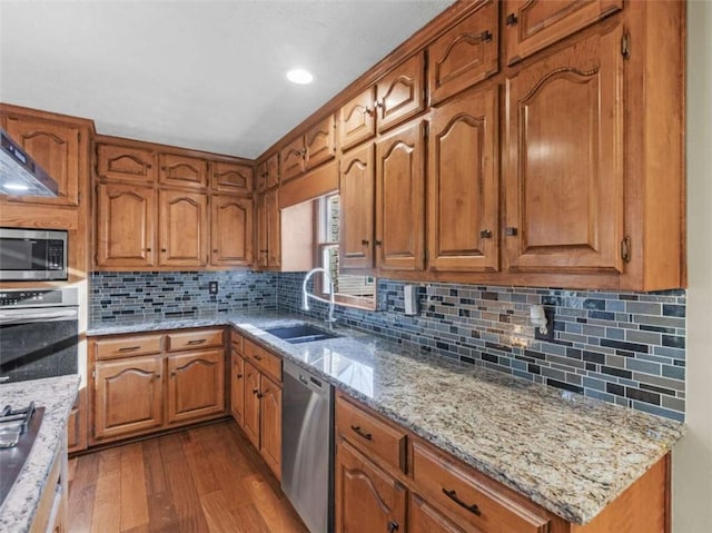 kitchen featuring stainless steel appliances, a sink, light stone countertops, brown cabinetry, and dark wood-style flooring