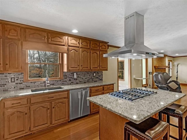 kitchen featuring light stone counters, a sink, island range hood, light wood-style floors, and appliances with stainless steel finishes