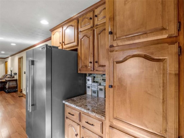 kitchen with recessed lighting, ornamental molding, freestanding refrigerator, light wood-style floors, and stone counters