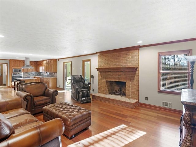 living area with light wood-style flooring, visible vents, recessed lighting, a brick fireplace, and crown molding