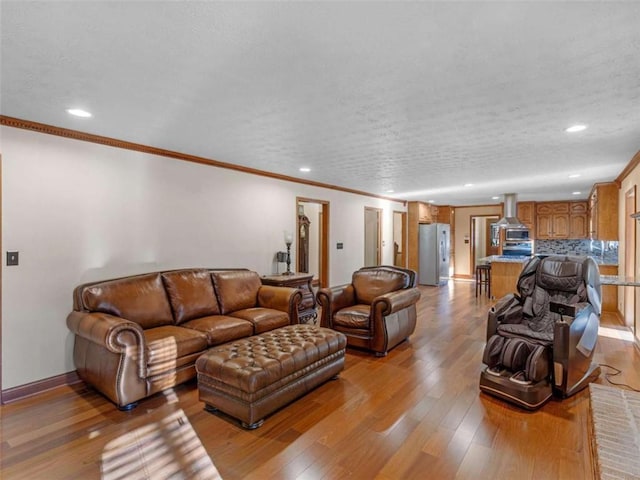 living room featuring light wood finished floors, a textured ceiling, baseboards, recessed lighting, and crown molding