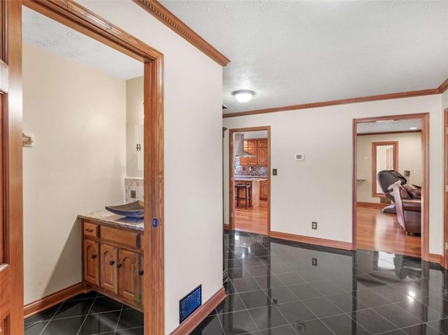 hall featuring baseboards, a textured ceiling, and crown molding
