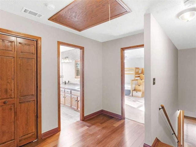 corridor with attic access, light wood finished floors, an upstairs landing, and visible vents