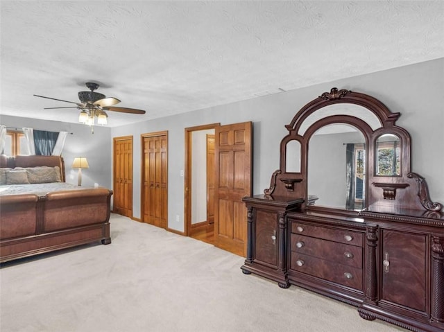 bedroom featuring light colored carpet, ceiling fan, multiple closets, and a textured ceiling