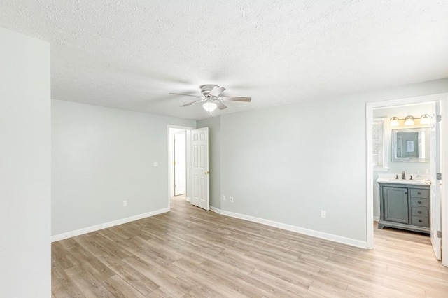 unfurnished room featuring ceiling fan, light wood-type flooring, sink, and a textured ceiling