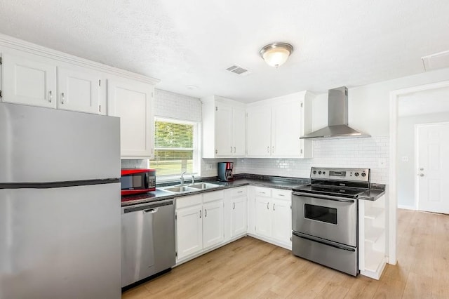 kitchen featuring wall chimney range hood, light hardwood / wood-style floors, sink, appliances with stainless steel finishes, and white cabinets