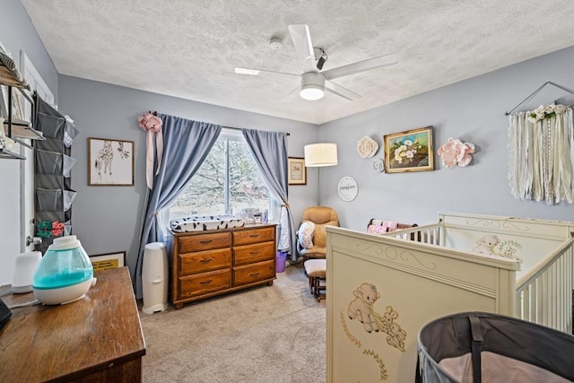 carpeted bedroom featuring a textured ceiling, a crib, and ceiling fan