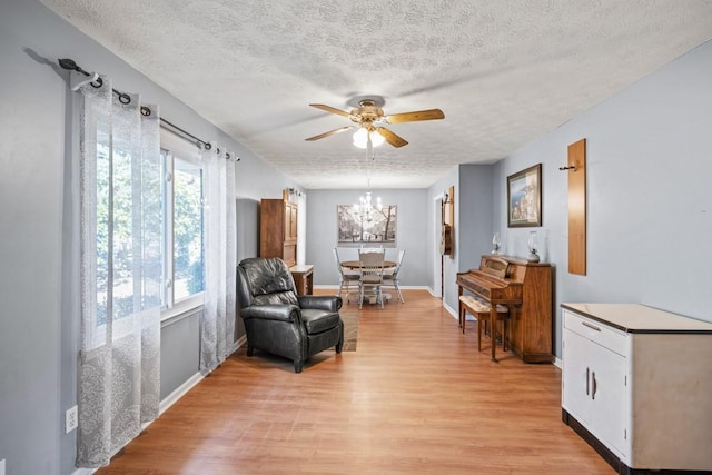 living area with ceiling fan with notable chandelier, a textured ceiling, and light hardwood / wood-style floors