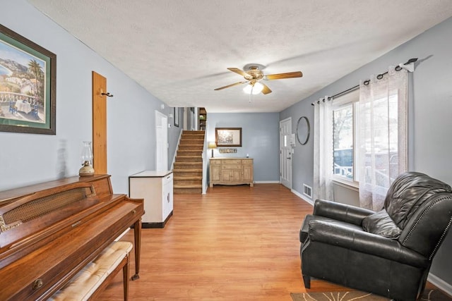 living area with ceiling fan, light hardwood / wood-style floors, and a textured ceiling