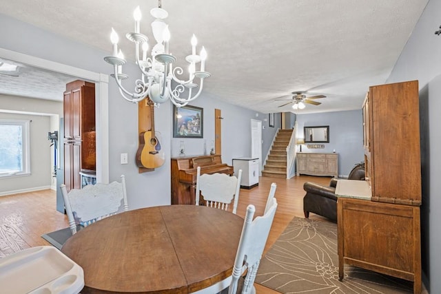 dining space with ceiling fan with notable chandelier, a textured ceiling, and light hardwood / wood-style floors