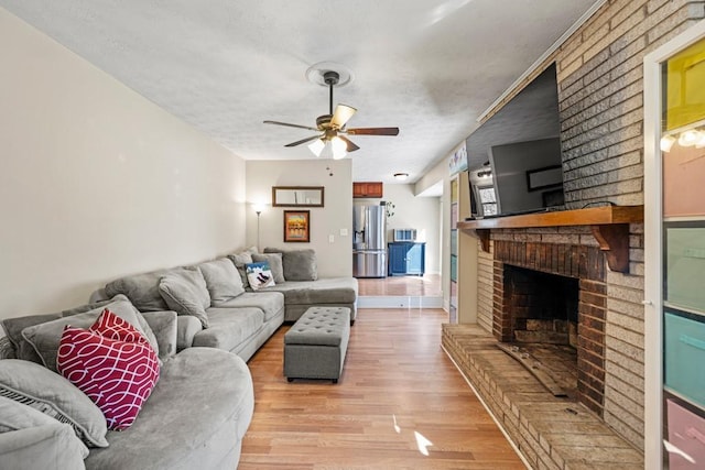 living room with ceiling fan, a textured ceiling, a brick fireplace, and light wood-type flooring