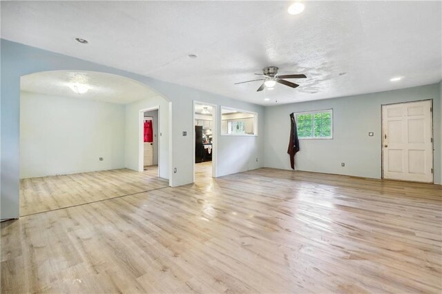 unfurnished living room with arched walkways, ceiling fan, and light wood-style floors