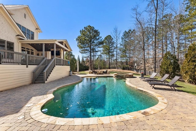 view of swimming pool with stairway, fence, a pool with connected hot tub, a sunroom, and a patio area