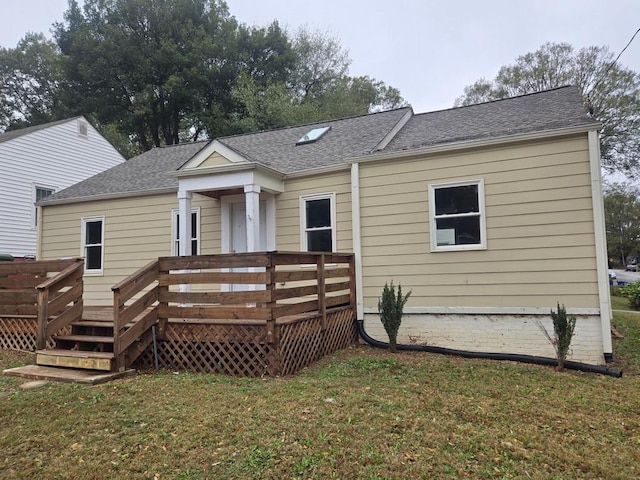 rear view of house featuring roof with shingles, a lawn, and a wooden deck