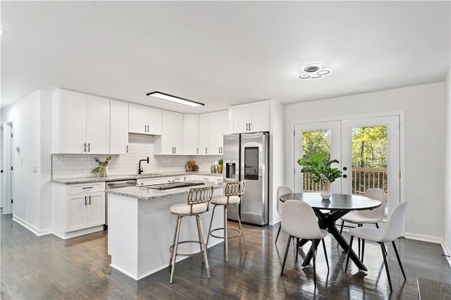 kitchen featuring stainless steel refrigerator with ice dispenser, decorative backsplash, light stone countertops, a kitchen island, and white cabinetry