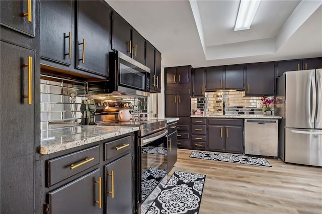 kitchen featuring sink, stainless steel appliances, tasteful backsplash, light hardwood / wood-style flooring, and a tray ceiling