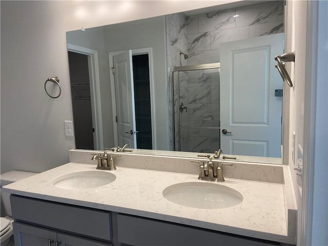 bathroom with a walk in closet, double vanity, a stall shower, and a sink