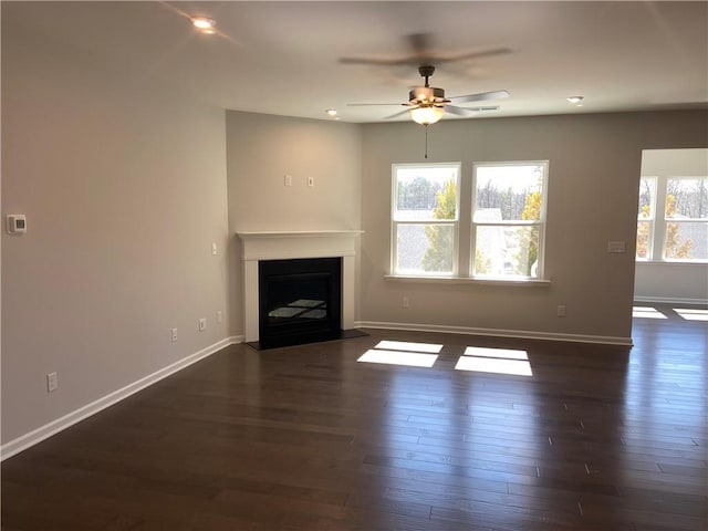 unfurnished living room featuring a wealth of natural light, ceiling fan, and dark wood-style flooring