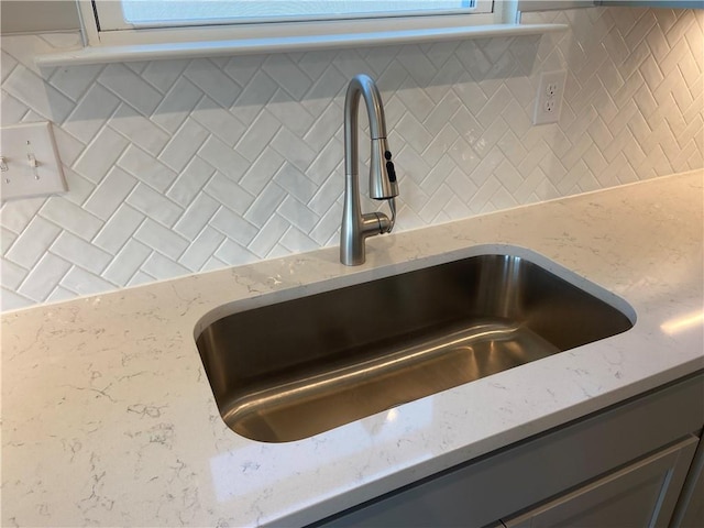 interior details with a sink, decorative backsplash, and light stone countertops