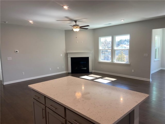 kitchen with dark wood finished floors, light stone counters, a fireplace with flush hearth, and ceiling fan