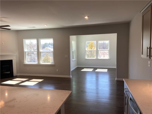 unfurnished living room featuring a wealth of natural light, baseboards, dark wood-type flooring, and a ceiling fan