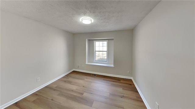 empty room featuring a textured ceiling, baseboards, and wood finished floors