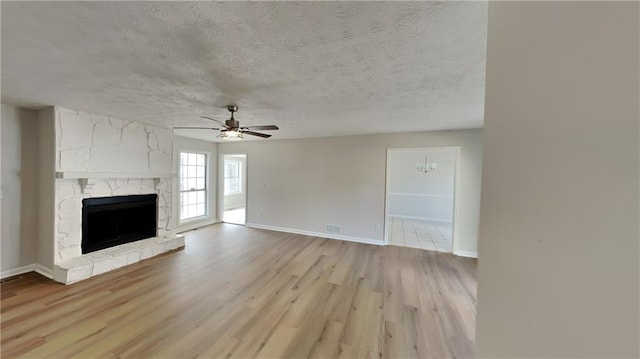 unfurnished living room with light wood finished floors, ceiling fan, a fireplace, and a textured ceiling