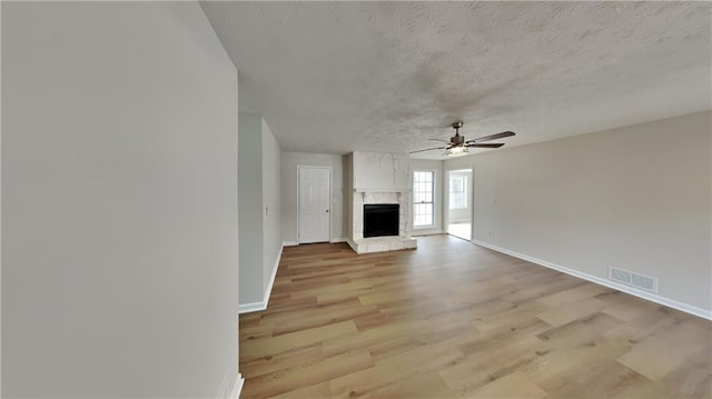 unfurnished living room featuring light wood finished floors, a fireplace, visible vents, and baseboards