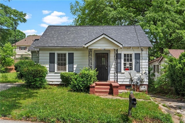 view of front of house with roof with shingles and a front yard
